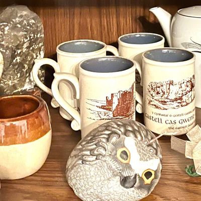 Assorted vintage ceramics, including a white teapot, Welsh castle souvenir mugs, a German-style beer stein, and a decorative owl figurine...
