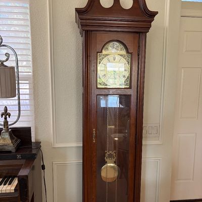 Sale Photo Thumbnail #85: Traditional grandfather clock in a dark wood case, featuring a swan neck pediment, ornate brass dial, and visible pendulum behind a glass door.