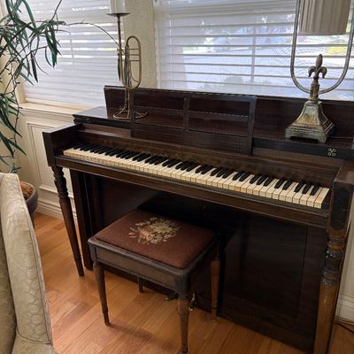 Sale Photo Thumbnail #84: Vintage dark wood upright piano with matching bench featuring a floral needlepoint cushion, showing some wear consistent with age.