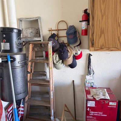 Sale Photo Thumbnail #27: Assorted garage items including a wooden stepladder, a central vacuum unit, a wall-mounted hat rack with baseball caps, and a boxed Home Accents Holiday iridescent reindeer decoration.