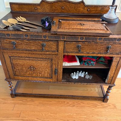 Sale Photo Thumbnail #71: Antique Jacobean revival oak sideboard featuring barley twist legs, carved geometric details, and drop-pull hardware, shown with loose parts and serving utensils on top.