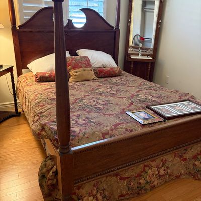 Sale Photo Thumbnail #36: Traditional four-poster wooden bed frame with a decorative headboard, dressed in floral bedding, shown alongside a matching wooden hall tree mirror in the background.