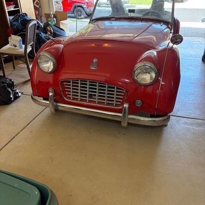 Sale Photo Thumbnail #14: Vintage red Triumph TR3 roadster convertible parked in a garage, featuring classic chrome grille and bumper details.