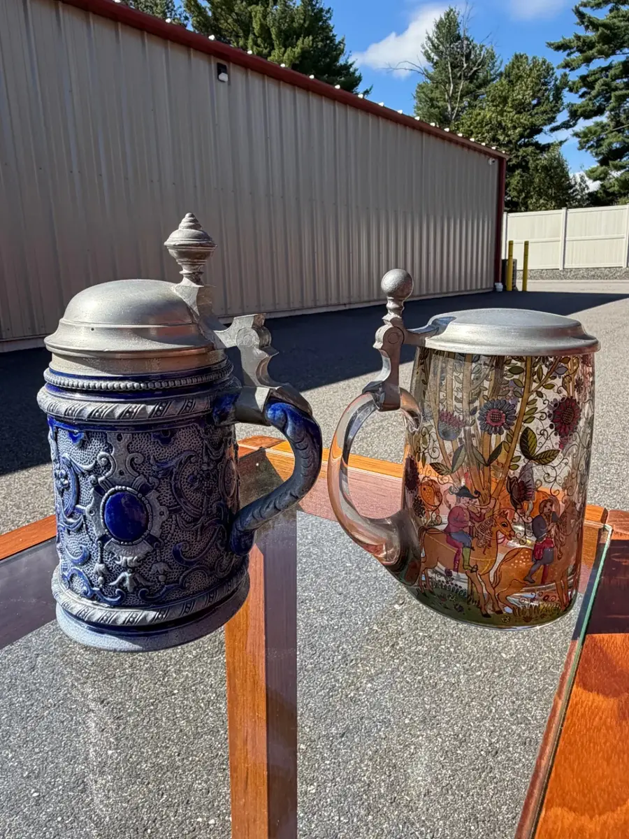 Two distinct styles of traditional German beer steins featuring classic mid-to-late 20th-century