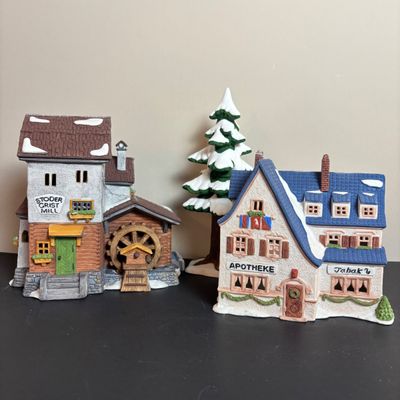 LOT 97: Dept 56 Alpine Village Series: Stoder Grist Mill, Apotek & Tabak along with a Village Porcelain Pine Tree