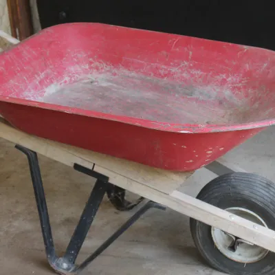 Vintage red metal wheelbarrow with wooden handles and a single rubber tire, showing some wear and tear from use.
