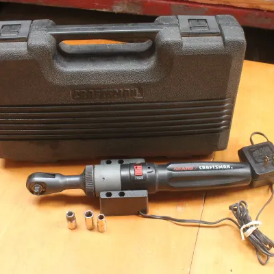 Vintage Sears Craftsman cordless power ratchet with three sockets, charging adapter, and original black plastic carrying case.