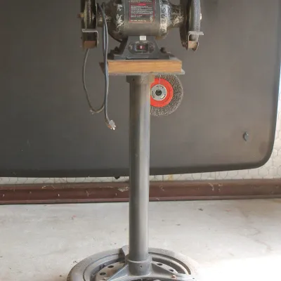 Vintage Craftsman bench grinder with integrated work light, mounted on a custom pedestal stand with a tire base.