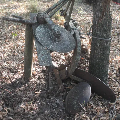 Vintage horse-drawn or tractor-drawn single-bottom disc plow, showing heavy rust, lichen growth, and weathering from outdoor storage.