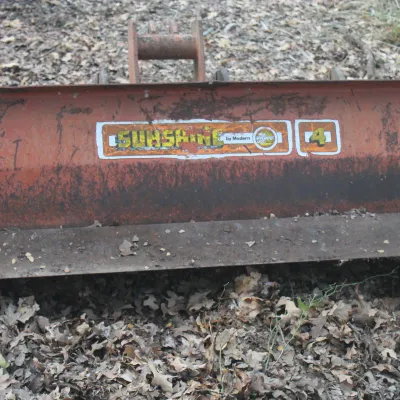 Vintage Sunshine by Modern 4-foot box blade tractor attachment, showing wear and rust from outdoor use.