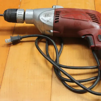 Vintage corded power drill with a red and silver magnesium housing, showing some wear from use.