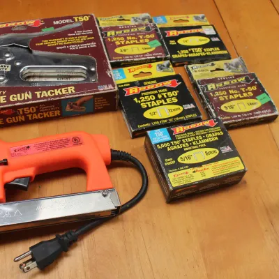 Arrow electric staple gun in bright orange, accompanied by a vintage Arrow T50 manual staple gun in its original box and several boxes of...