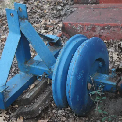 Blue painted three-point hitch attachment with a trailer ball and heavy-duty dual pulleys, showing some wear and rust from outdoor storage.