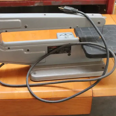 Vintage Dremel Model 571 scroll saw with a grey metal housing and black work table, showing some light wear from use.