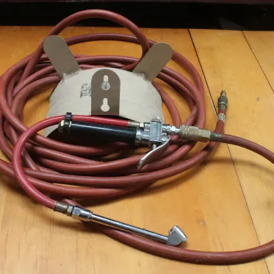 Coiled red rubber air hose with a tire inflator attachment and a wall-mountable metal hose hanger.