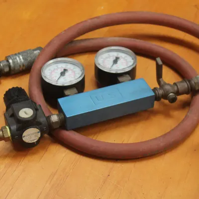 Pneumatic pressure regulator assembly with dual pressure gauges, a blue manifold block, and an attached red air hose.