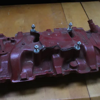 Vintage cast iron intake manifold painted red, featuring four mounting studs and a vertical oil fill tube.