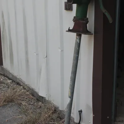 Vintage cast iron pitcher pump with green paint, mounted on a long galvanized pipe.