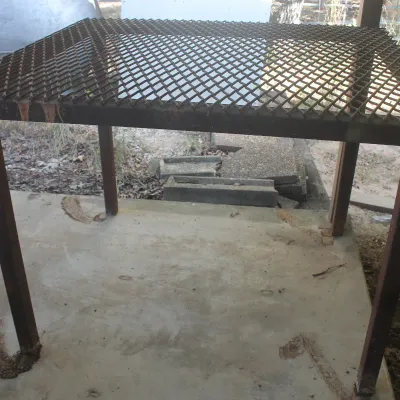 Heavy-duty welded metal work table with an expanded metal mesh top and square tube legs, showing some surface rust.