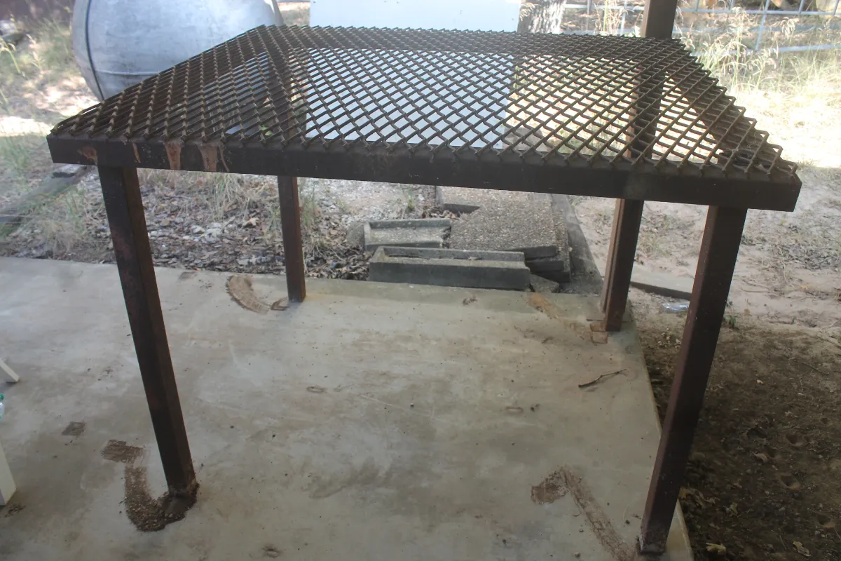 Sale Photo Thumbnail #113: Heavy-duty welded metal work table with an expanded metal mesh top and square tube legs, showing some surface rust.