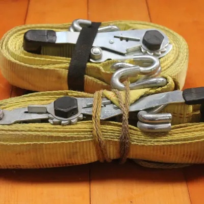 Pair of heavy-duty yellow ratchet tie-down straps with metal hooks, showing light wear from use.