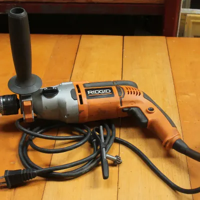 Ridgid corded hammer drill with auxiliary handle and chuck key, showing some signs of use.