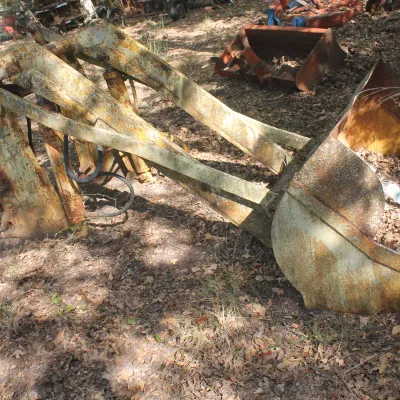 Vintage tractor front-end loader attachment with bucket, showing significant rust and weathering from outdoor storage.