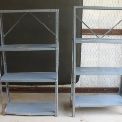 Two grey metal utility shelving units, showing some wear and tear from garage or workshop use.