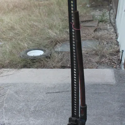 Vintage high-lift farm jack with a black steel bar and a red handle, showing some wear and surface rust from outdoor use.