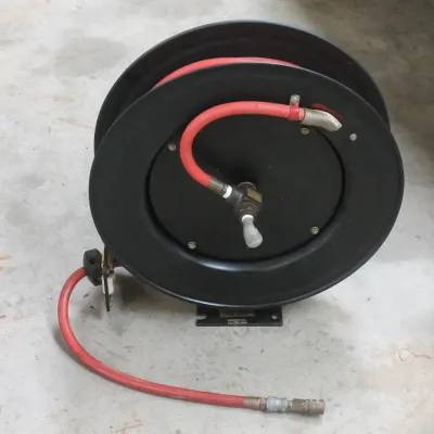 Heavy-duty retractable air hose reel with a black metal casing and a red rubber hose, showing light wear from workshop use.