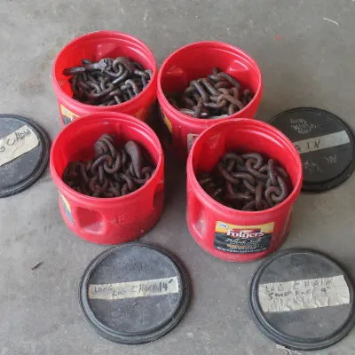 Four heavy-duty log chains of varying lengths, stored in red Folgers coffee canisters with labeled black lids.