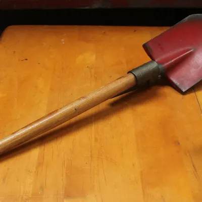 Vintage military-style folding entrenching shovel with a red-painted metal blade and a wooden handle.
