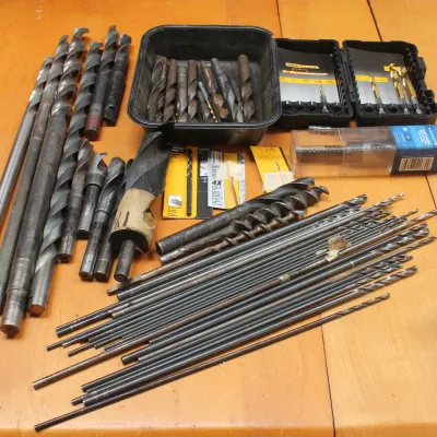 Assortment of vintage and modern drill bits, including extra-long installer bits, masonry bits, and packaged sets, showing signs of use.