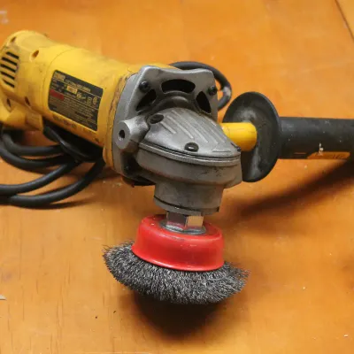 DeWalt corded angle grinder with side handle and wire cup brush attachment, showing signs of moderate use.