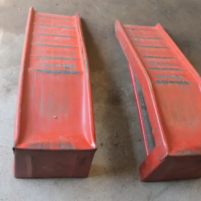Pair of vintage red painted steel car ramps, showing some wear and paint loss from use.