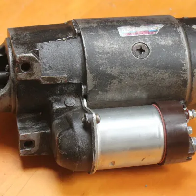 Vintage automotive starter motor with attached solenoid, showing some wear and cosmetic aging.