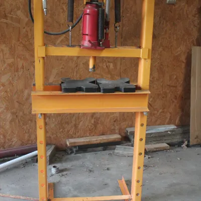 Yellow H-frame hydraulic shop press with a red bottle jack, showing some signs of use.