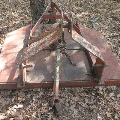 Vintage pull-behind rotary cutter attachment for a tractor, showing significant rust and wear from outdoor storage.