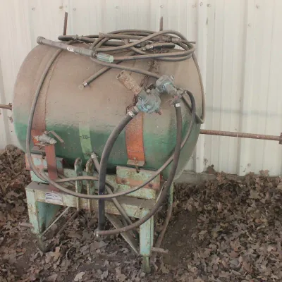 Vintage pull-behind agricultural sprayer tank with hoses and pump assembly, showing heavy wear and rust from outdoor storage.