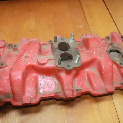 Vintage Chevrolet cast iron intake manifold painted red, featuring casting number 3704784, suitable for a 265 cubic inch V8 engine.