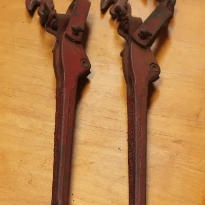 Pair of vintage red lever-type load binders with grab hooks, showing some wear and paint loss from use.