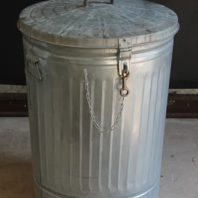 Vintage galvanized metal trash can with a matching lid, side handles, and a front chain lock mechanism.