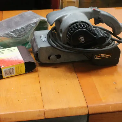 Vintage Craftsman belt sander with cast aluminum housing, accompanied by several replacement sanding belts.