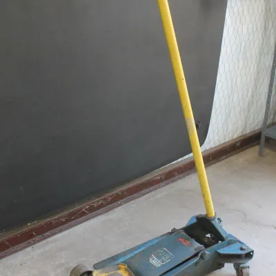 Vintage Walker blue hydraulic floor jack with a long yellow handle, showing signs of wear and use.