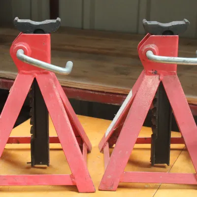Pair of red steel jack stands with adjustable ratcheting bars, showing some light wear from use.