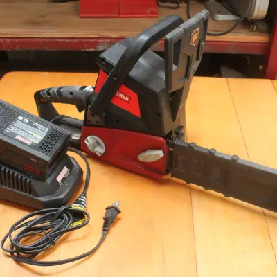 Craftsman cordless chainsaw with a protective blade cover, accompanied by a DieHard lithium-ion battery and charger.