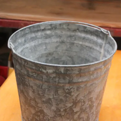 Vintage galvanized metal bucket with a wire bail handle, showing a weathered patina.
