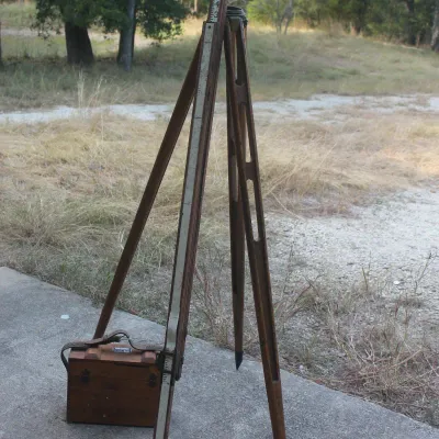 Vintage wooden surveyor's tripod, leveling rod, and matching wooden carrying case, showing wear consistent with age and use.