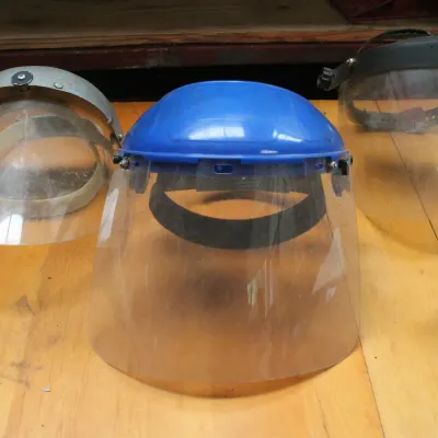 Three vintage industrial face shields with adjustable headbands, showing some wear and scuffs from use.