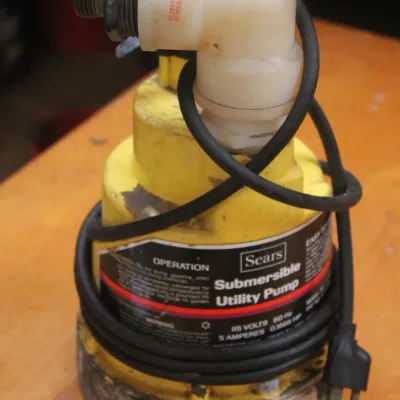 Vintage Sears yellow submersible utility pump with attached power cord and plastic elbow fitting, showing some wear from use.